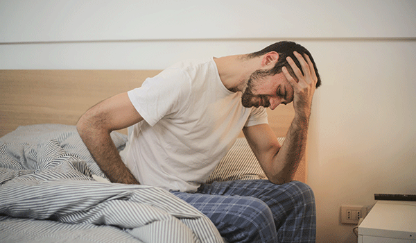 young man sat on bed in sleepwear suffering from headache